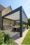 Pergola aluminium sur mesure adossée gris anthracite à lames orientables sur terrasse avec jardin fleuri