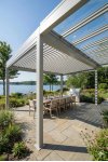 Pergola aluminium sur mesure adossée à lames orientables grises sur terrasse bois avec vue mer et stores latéraux
