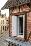Persienne bois blanche ouverte sur maison à colombages et briques en centre-ville