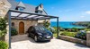 Carport aluminium à toit polycarbonate devant une maison en pierre – abri de voiture lumineux
