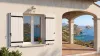 Volet battant PVC plein blanc à lames verticales et pentures noires sur une maison avec vue mer en bord de Méditerranée