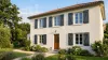 Volets battants PVC gris anthracite à barres et écharpe en Z sur une maison en enduit clair avec jardin fleuri