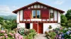 Volets battants PVC rouges à barres et écharpe sur une maison basque blanche à colombages, hortensias au jardin